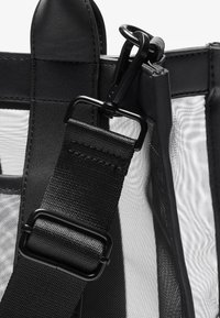 Bolsa preta com secções em malha, apresenta uma alça texturada e um fecho de metal; acabamentos em couro liso e um design elegante e estruturado.