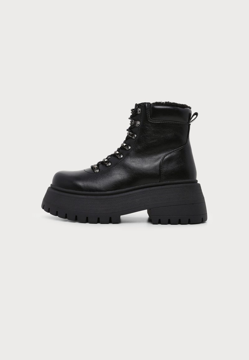 Bottine noire en cuir avec semelle plateforme épaisse, lacets à l'avant avec œillets métalliques et col rembourré sur fond blanc.