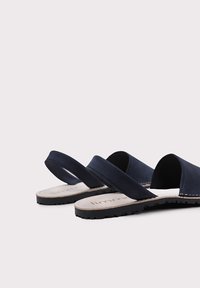 Sandalias azul marino con dos correas anchas, parte superior de cuero, suela de goma y detalles de costura en el borde. Diseño en la parte posterior abierta para facilitar su uso.