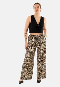 Top negro corto con detalle de lazo, combinado con pantalones de leopardo de pierna ancha con cintura ajustable. Tejido suave, patrón audaz.
