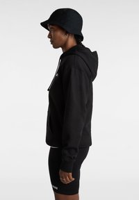 Zwarte hoodie met trekkoorden, gestructureerde stof, zijzakken, gecombineerd met zwarte shorts en een zwarte bucket hat. Eenvoudig ontwerp.
