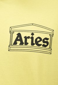 Tissu jaune avec un graphisme en contour noir ressemblant à un temple grec et le mot « Aries » en police stylisée en gras à l'intérieur.
