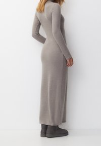 Robe en tricot grise à manches longues et côtelées avec un col haut, silhouette ajustée, atteignant le mollet, accompagnée de bottes de cheville grises.