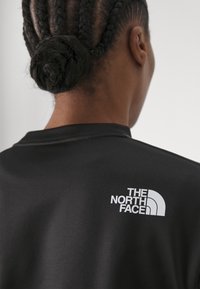 Maglietta sportiva nera con un logo bianco sulla parte superiore della schiena. Il materiale sembra liscio e aderente, con un collo a giro.