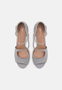 Silver glitter sandals with open toe, wide straps, and ankle buckle. Smooth inner lining and subtle shine enhance overall design.