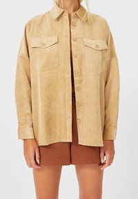 Lys beige corduroy skjorte med to brystlomme, knappelukning foran og justerbare ærmekanter. Kombineret med brune shorts.