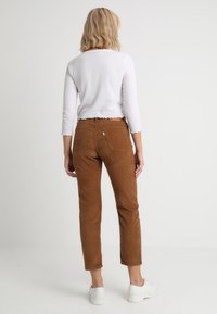 Pantalon en velours côtelé marron à coupe droite, doté de deux poches arrière et d'une fermeture à bouton, associé à un haut à manches longues blanc.