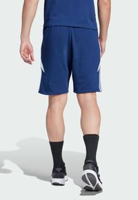 Mørkeblå sportsshorts med hvide sidelogoer, der har en elastisk talje og en afslappet pasform, samt sorte ankelstrømper og sneakers.
