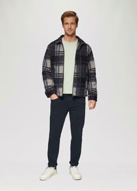 Karierte Flanelljacke in Marineblau, Grau und Weiß, kombiniert mit einem mintgrünen Hemd und dunklen Hosen. Weiße Sneakers runden das Outfit ab.