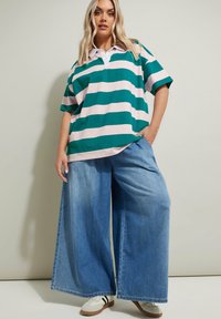 Grön och rosa randig oversized polo shirt med vit krage, i kombination med vida ljusblå denimjeans och vita sneakers med svarta ränder.