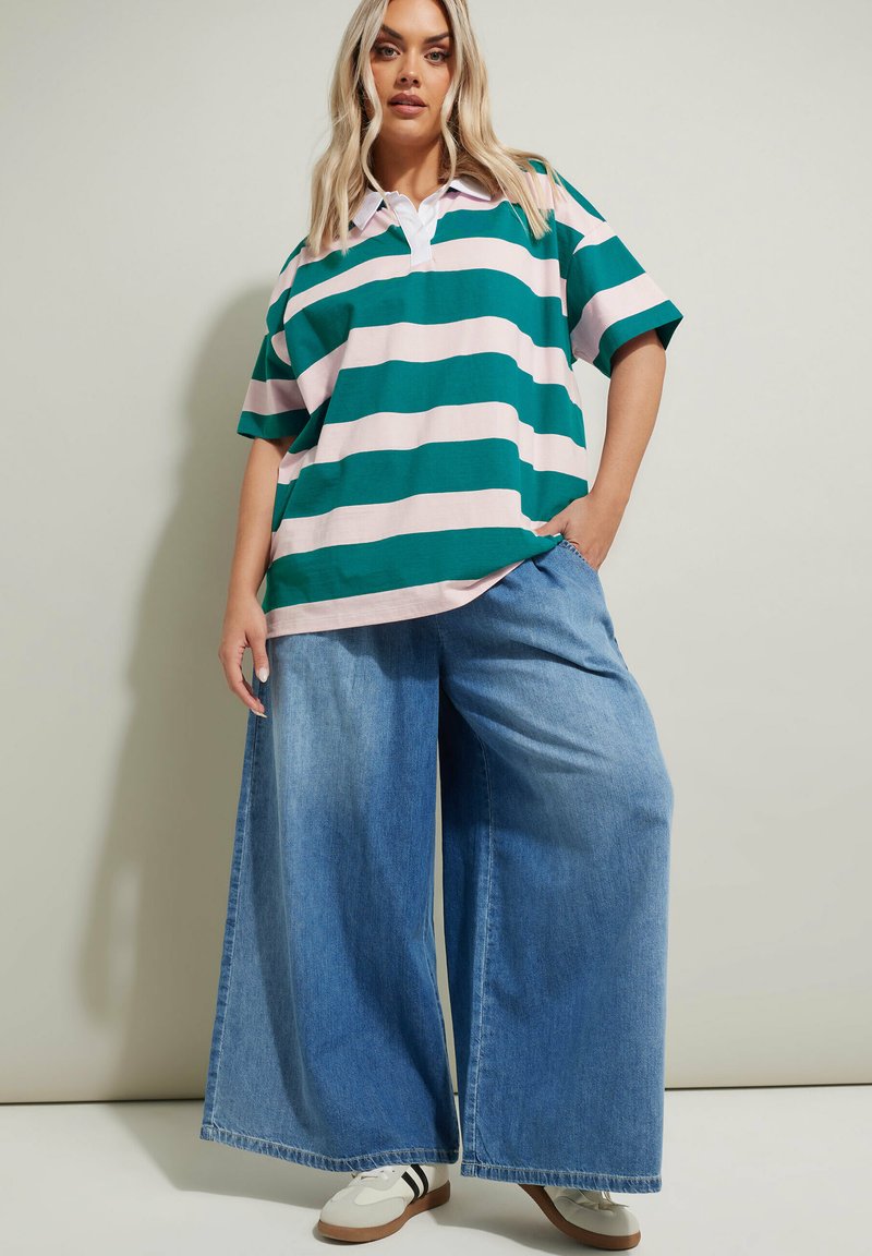 Grön och rosa randig oversized polo shirt med vit krage, i kombination med vida ljusblå denimjeans och vita sneakers med svarta ränder.