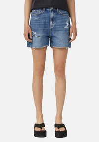 Shorts en denim bleu moyen avec des détails déchirés, un ourlet effiloché et un design à cinq poches, associés à des sandales à plateforme.