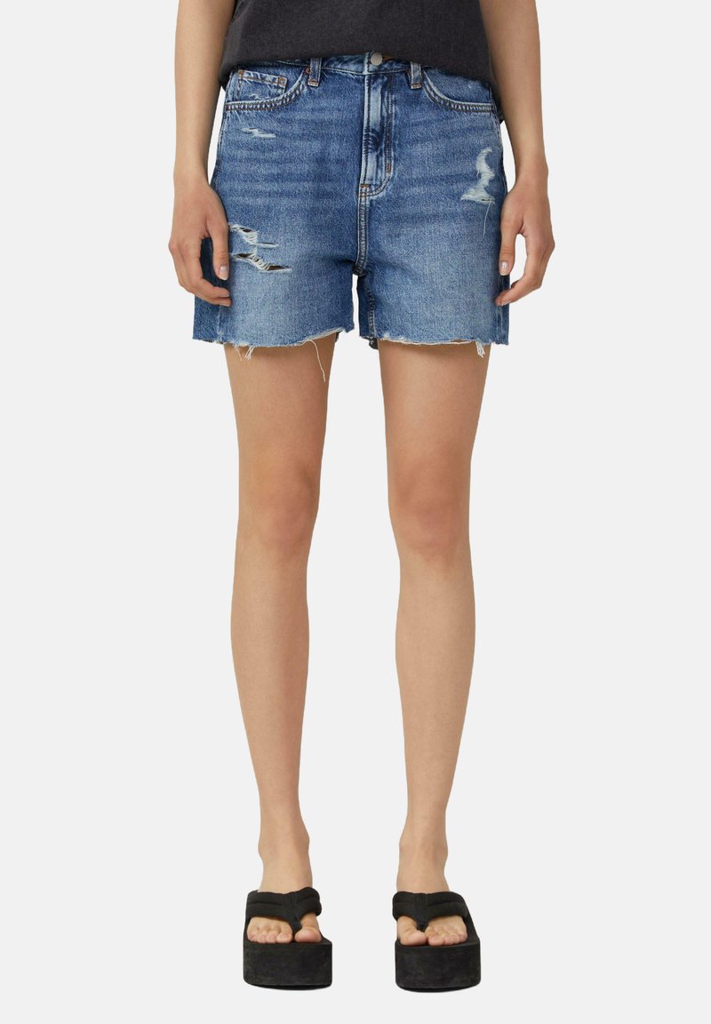 Shorts en denim bleu moyen avec des détails déchirés, un ourlet effiloché et un design à cinq poches, associés à des sandales à plateforme.