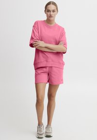 Lyserød bomulds oversized sweatshirt parret med matchende shorts, der har en afslappet pasform og enkelt design, båret med lyse sneakers.