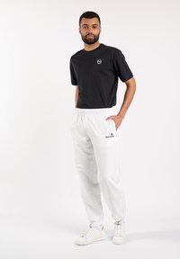 Zwart T-shirt met korte mouwen en ronde hals met logo, gecombineerd met witte joggers met elastische tailleband voorzien van een logo en boorden; gedragen met witte sneakers.