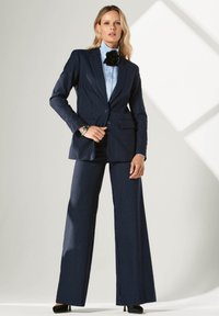 Marineblauer Nadelstreifenanzug, bestehend aus einem taillierten Blazer und weiten Hosen mit Knopfverschluss und zwei vorderen Taschen, kombiniert mit einer hellblauen Bluse.
