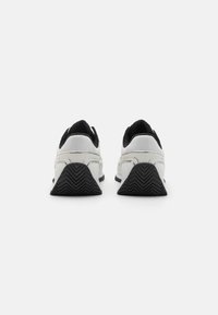 Baskets de sport blanches avec des accents noirs, présentant une semelle texturée, une surface lisse et un col rembourré pour le confort.