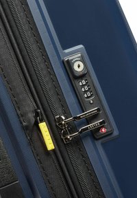 Valigia rigida blu marina con zip nera e etichetta gialla. Dotata di lucchetto TSA con codice numerico e tirazip argentati.
