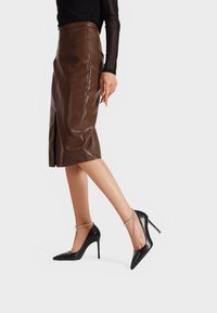 Décolleté neri con tacco alto, punta affusolata, finitura in pelle liscia e una cinghia decorativa alla caviglia con piccole perline trasparenti.