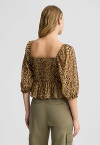 Bluza s uzorkom životinja u smešnim i bež tonovima, s puf rukavima, smock bodicom i peplum rubom, kombinirana s cargo hlačama u maslinastozelenoj boji.