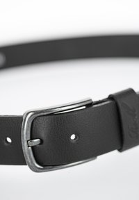 Cinturón de cuero negro con superficie texturizada, hebilla de metal plateado y múltiples agujeros para ajuste. Cuenta con una etiqueta de cuero de marca.