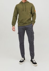Olivgrüner Kapuzenpullover mit Fronttasche, graue Cargo-Hosen mit Seitentaschen und schwarze Sneakers mit weißen Sohlen. Glatte Stofftextur.