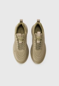 Baskets khaki avec une tige en maille texturée, bout rond et lacets ton sur ton. Comprend une languette et un design superposé sur la semelle extérieure.