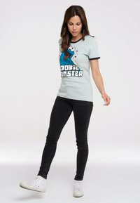 Light blue cotton t-shirt with black trim, featuring a colorful Cookie Monster graphic. Paired with black skinny jeans and white sneakers.