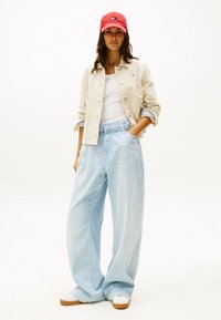 Pantalones anchos de rayas azul claro con cintura alta, combinados con una chaqueta crema de botones y una gorra roja, junto con zapatillas blancas.