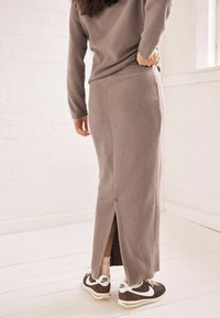 Grå strikket maxi-nederdel med en sideslids og blød tekstur, parret med brune og hvide sneakers. Ensemblen har en afslappet silhuet.