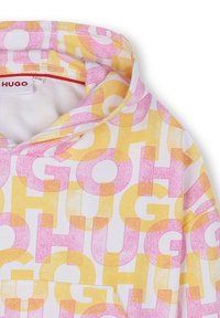 Haut à capuche blanc avec un grand lettrage "HUGO" en rose et jaune dans différentes orientations. Tissu doux avec une poche kangourou et un cordon de serrage pour la capuche.