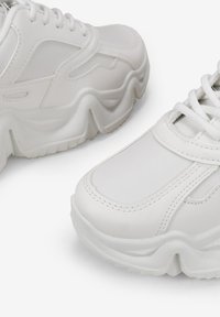 Zapatillas blancas voluminosas que presentan una combinación de material sintético liso y acentos texturizados, con suelas gruesas y múltiples detalles de costura.