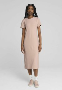 Robe rose à manches courtes avec une texture côtelée et une coupe droite, atteignant le mi-mollet. Associée à des baskets légères et des chaussettes blanches.