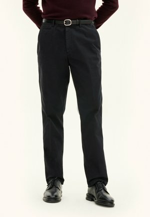 Black, straight-leg trousers made of cotton with a smooth texture, featuring side pockets and a button closure, paired with black leather shoes.