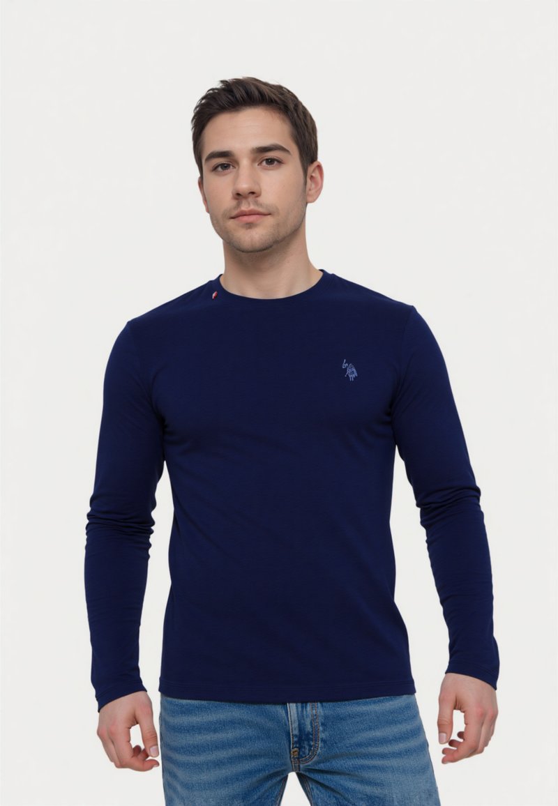 Maglietta a maniche lunghe blu navy realizzata in tessuto morbido con scollatura rotonda. Presenta un piccolo logo sul petto e un accento rosso sulla spalla.