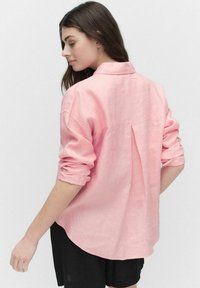 Roze linnen shirt met een kraag, opgerolde mouwen en een rugplooi. Afgeronde zoom met een losse pasvorm, gecombineerd met zwarte shorts.