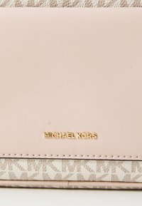 Růžová kožená peněženka s texturovaným látkovým dnem, s zlatým logem "MICHAEL KORS" a geometrickým vzorem v neutrálních tónech.