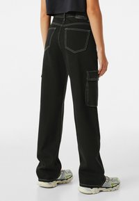 Svarta cargobyxor med vit söm, fyra fickor, lös passform och lätt utsvängda vid ankeln. Materialet verkar tåligt.