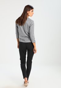 Suéter riscado em preto e branco com mangas três quartos, combinado com calças pretas ajustadas, usado com sapatos planos bege.