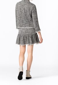 Svart och vit tweedjacka med en figursydd design, i kombination med en utsvängd kjol. Båda plagg har fransade kantar och textil med struktur. Lätta stövlar fulländar looken.