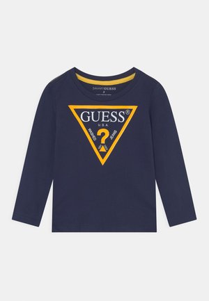 Marineblå langærmet skjorte med en gul trekantslogo med ordet GUESS, et spørgsmålstegn og teksten "WASHED JEANS."