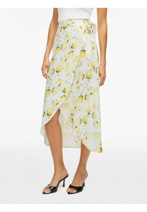 Kvinde iført en hvid slåom-nederdel med et mønster af gule citroner og grønne blade, kombineret med sorte åbne hæle-sandaler.