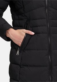 Sort puffjakke med quiltet struktur, der har lynlåslukning og sidelomme. Stoffet er glat og let skinnende.
