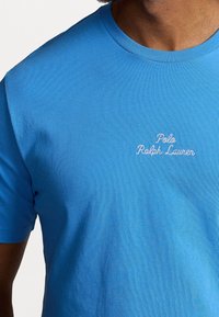 Blue cotton t-shirt with a crew neckline, featuring embroidered white text "Polo Ralph Lauren" on the chest. Smooth texture, fitted design.