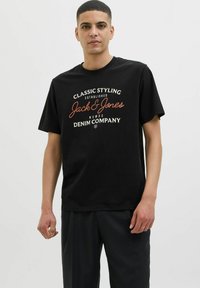 Melna kokvilnas T-krekls ar baltu un oranžu grafiku, kurā izcelti "Jack & Jones" un citi zīmola elementi.