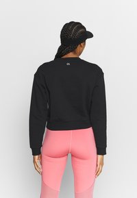 Sweatshirt noir court avec des manches longues, présentant un petit logo blanc à l'arrière. Associe avec des leggings roses qui possèdent des panneaux en bloc de couleurs.