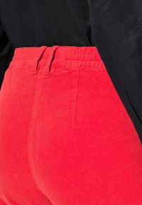 Červené kordové kalhoty s texturovaným povrchem, s páskem na elastickou gumu a viditelnými švy. Doplněné černým topem.