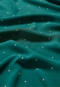 Tela verde azulado con una textura suave, presenta lunares blancos distribuidos uniformemente por toda la superficie, dispuestos en un patrón delicado.