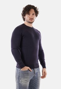 Maglione in maglia blu navy con scollatura tonda e maniche lunghe, realizzato in un tessuto liscio. Abbinato a jeans chiari strappati.