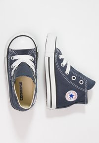 Marineblaue Canvas-Hochtop-Sneaker mit weißen Schnürsenkeln, gummierter Zehenschutzkappe und schwarzem Streifen. Mit runder Logopatch an der Seite.